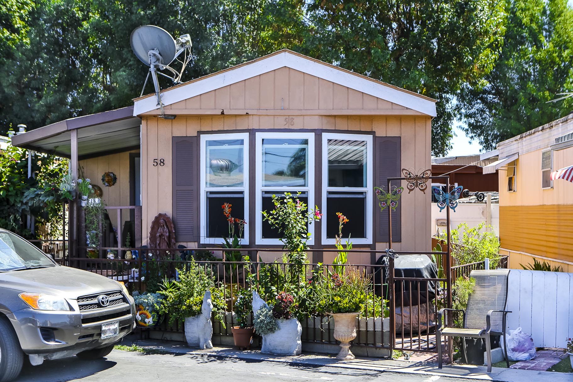 tan mobile home surrounded by green plants and trees in Bellflower, CA